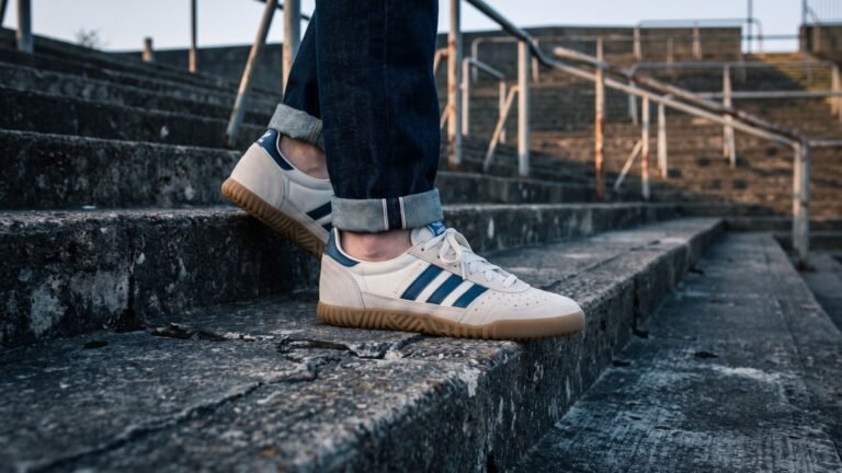 Person wearing cream and blue Adidas Indoor Super sneakers descending concrete stadium terrace steps