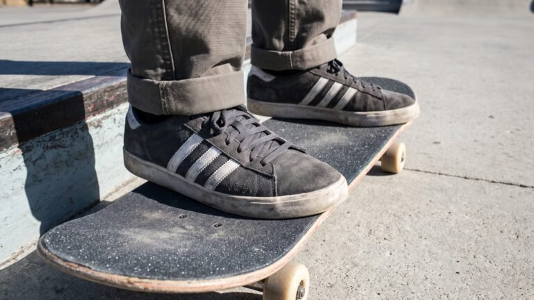 Skater wearing grey suede Adidas sneakers standing on a skateboard deck at an outdoor park