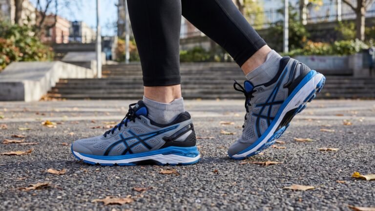 Runner wearing supportive grey and blue ASICS Gel-Kayano sneakers on a paved park path