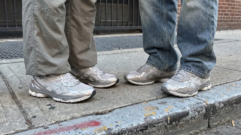 Two people wearing metallic silver Asics running sneakers with relaxed trousers on a city sidewalk