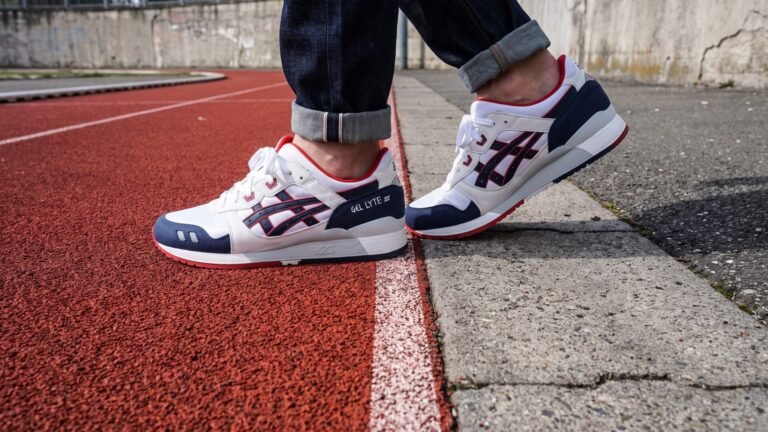 Asics Gel-Lyte III sneakers positioned across a red running track and a concrete sidewalk
