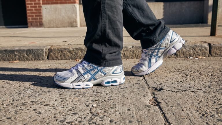 Silver and blue ASICS Gel-Nimbus 9 running shoes worn with dark pants on an urban concrete sidewalk