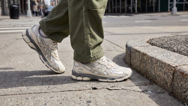 Person wearing cream and silver ASICS Gel-NYC sneakers walking on a city sidewalk