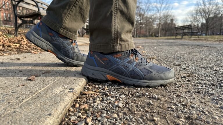 ASICS Gel-Venture 11 sneakers stepping from a paved curb onto a loose gravel park trail