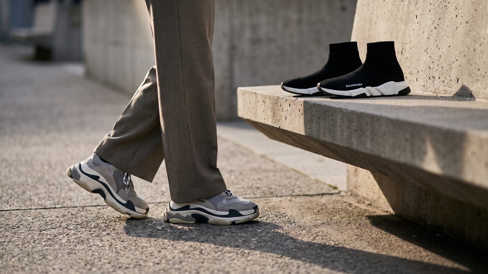Balenciaga Triple S sneakers worn with tailored trousers next to black Speed sock sneakers on a concrete bench
