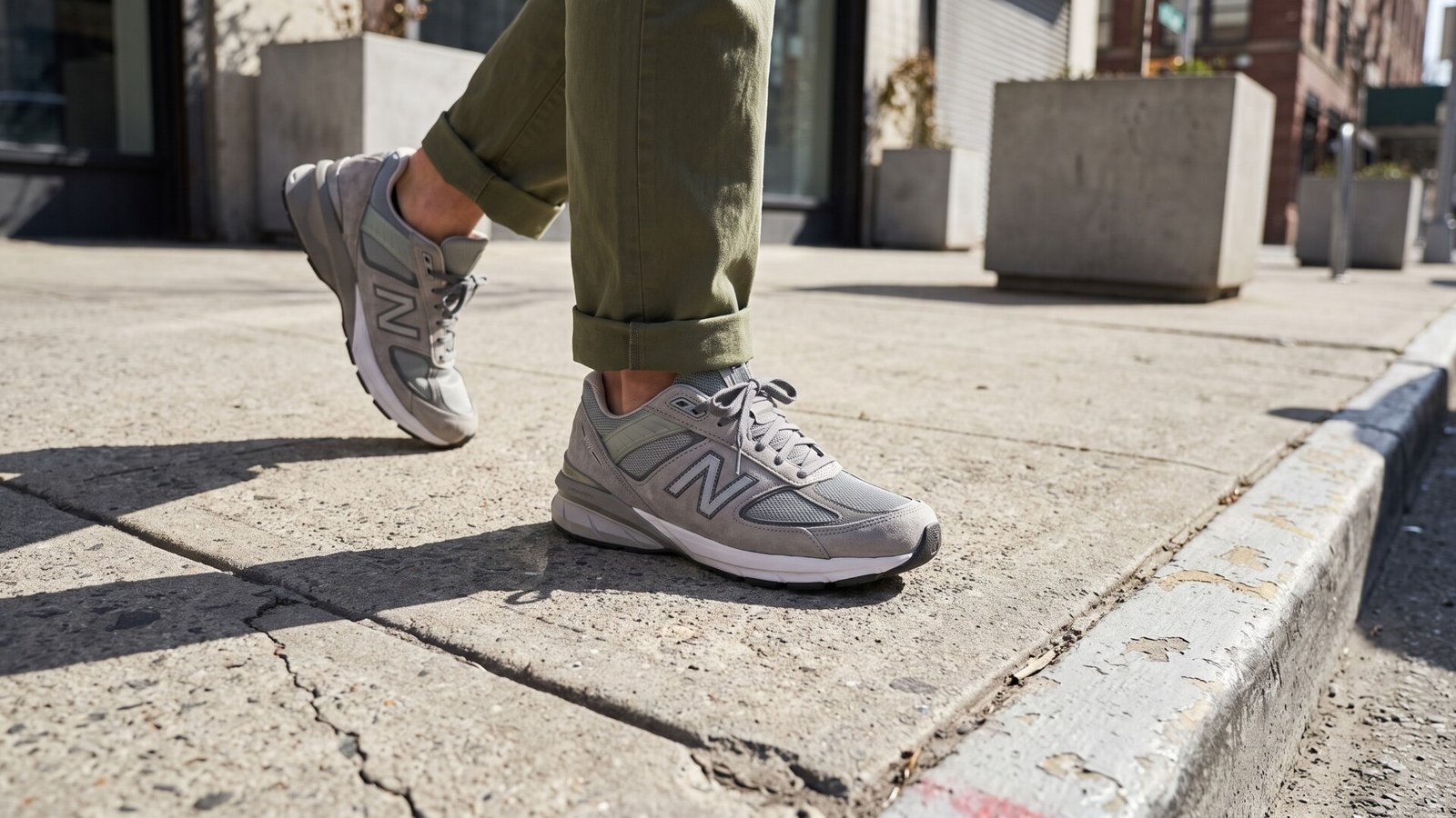 Close-up of a person wearing classic grey New Balance sneakers while walking along an urban sidewalk