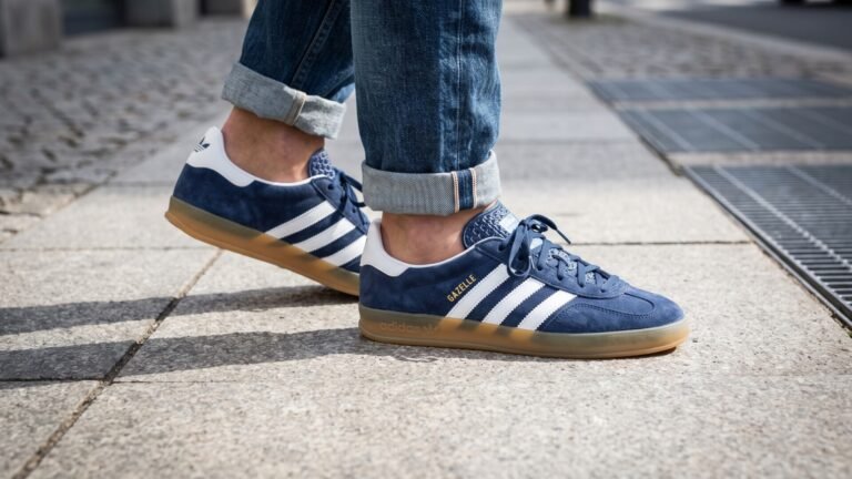 Person wearing blue suede Adidas Gazelle sneakers with gum soles and cuffed denim jeans on a sidewalk