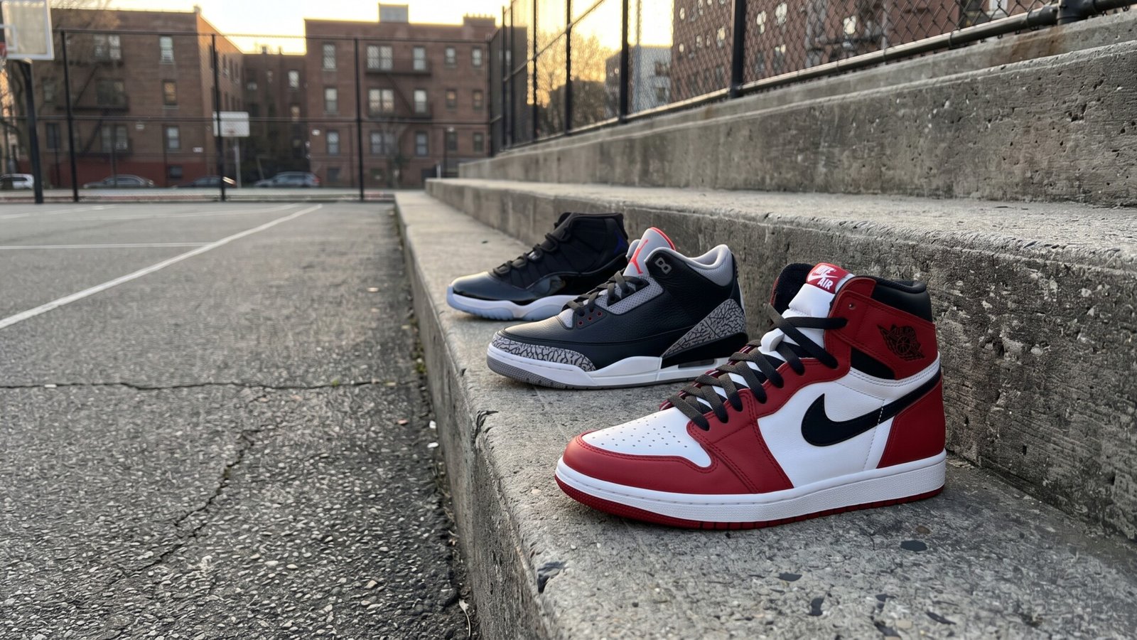 Three classic Air Jordan sneakers lined up on concrete bleachers beside an urban outdoor basketball court