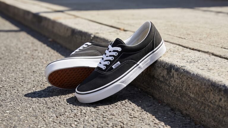 Pair of classic black canvas Vans Era sneakers resting against a concrete sidewalk curb