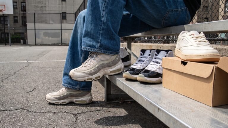 Person wearing Nike Air Max 95s seated next to Air Jordan 11s on an urban basketball court bleacher