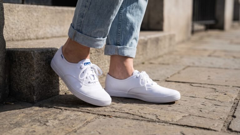 White low-profile Keds canvas sneakers worn with cuffed light-wash blue jeans on stone steps