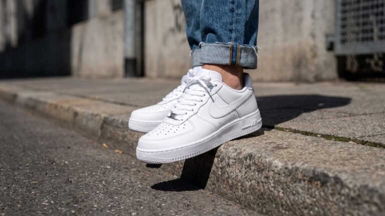 Classic all-white Nike Air Force 1 low sneakers worn with cuffed jeans on a city curb