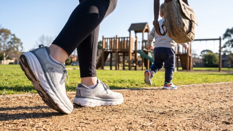 Close-up of a parent wearing cushioned grey sneakers walking behind a running toddler at a playground