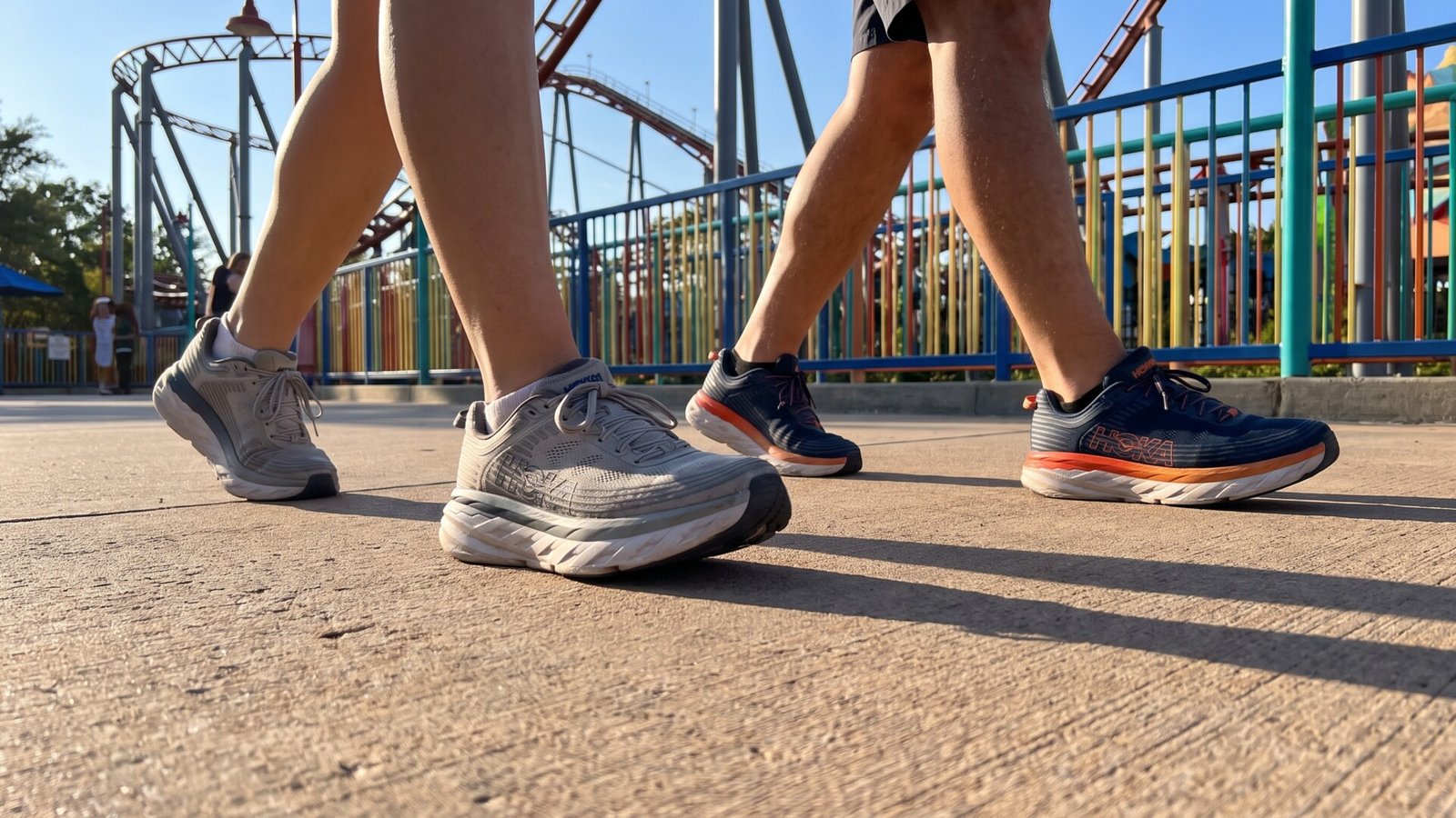 Two visitors wearing cushioned running sneakers walking past a roller coaster at a theme park