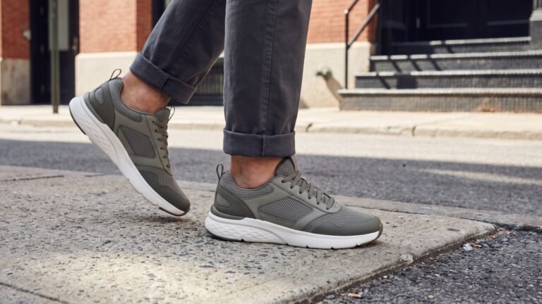 Person walking on an urban sidewalk wearing olive green mesh sneakers with cushioned white soles