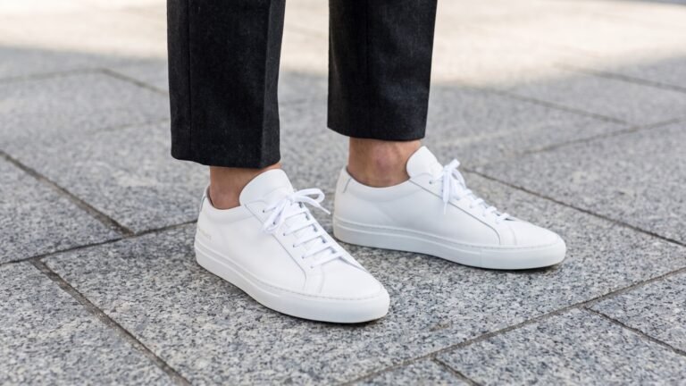 White leather Common Projects Achilles Low sneakers styled with cropped charcoal trousers outdoors