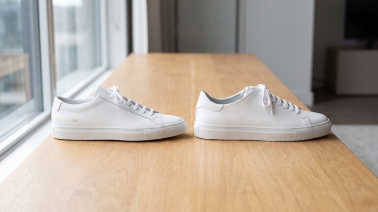 Common Projects Achilles Low and Axel Arigato Clean 90 white leather sneakers side by side on a wooden table
