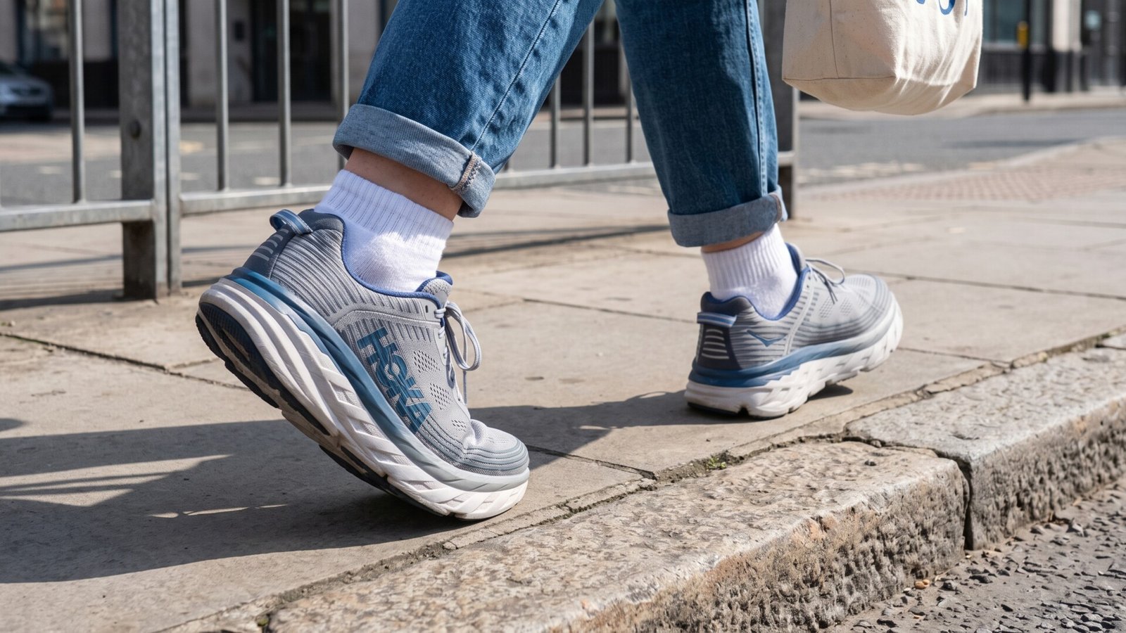 Pedestrian walking on a city sidewalk wearing supportive grey and blue cushioned sneakers and cuffed jeans