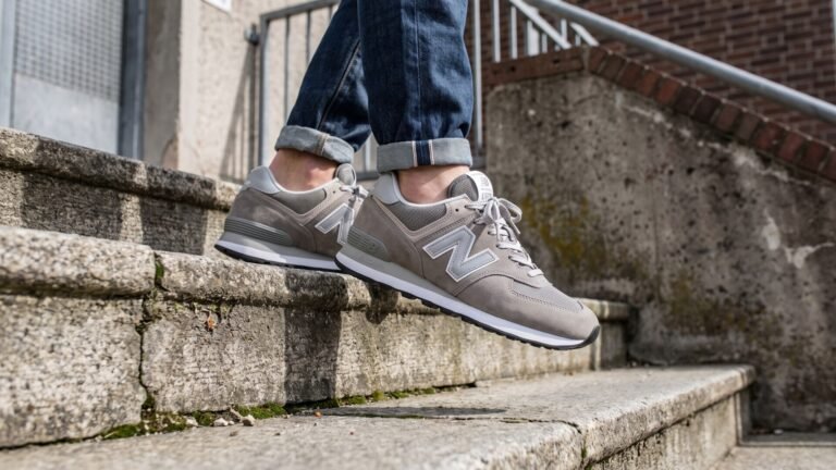 Classic grey suede and mesh New Balance 574 sneakers worn with cuffed jeans on concrete steps