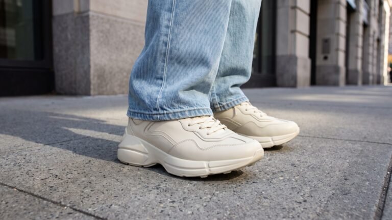 Off-white Gucci Rhyton chunky leather sneakers paired with light blue jeans on a paved city sidewalk