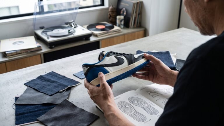 Designer hands inspecting a blue, black, and white sneaker prototype over technical sketches and fabric swatches