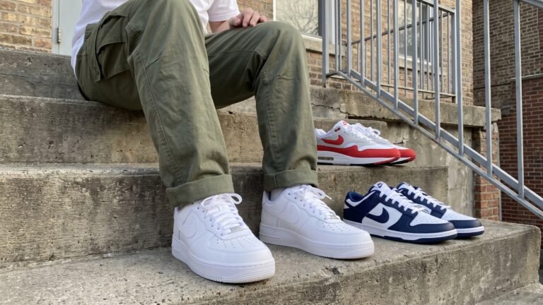 Person wearing white Nike Air Force 1s seated on concrete steps alongside Nike Dunk Lows and Air Max 1s