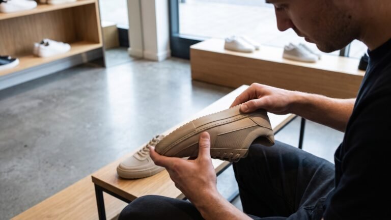 Shopper closely inspecting the sole and stitching of a beige low-top sneaker in a store