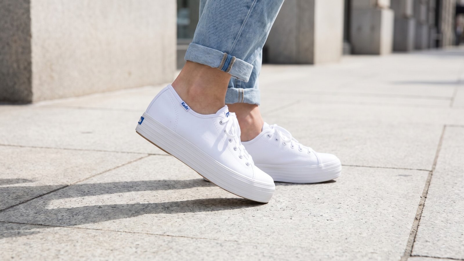 White canvas Keds Triple Kick platform sneakers styled with cuffed light-wash jeans on a sidewalk
