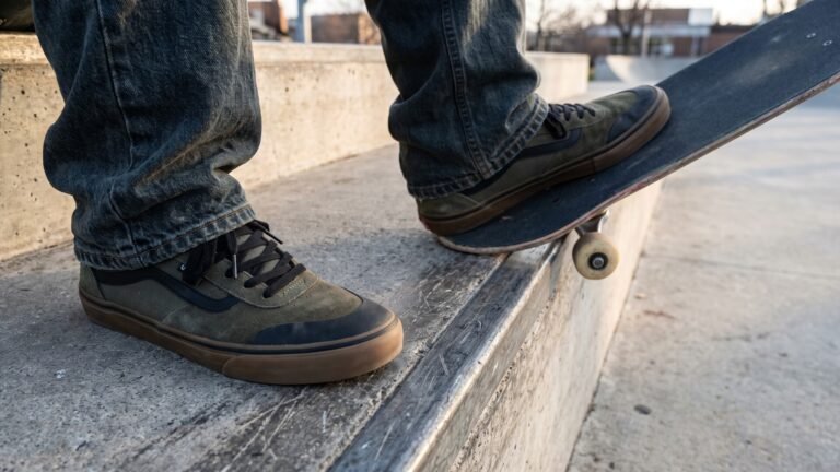 Skater in olive green suede skate sneakers with gum soles resting on a skateboard atop a concrete ledge