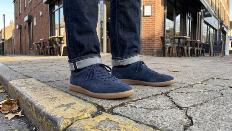 Navy blue suede terrace sneakers with gum soles worn with cuffed dark denim jeans on an urban pavement