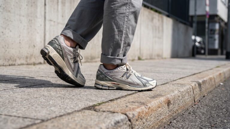 Side view of New Balance 1906R sneakers worn with cuffed grey trousers while walking on a paved city sidewalk