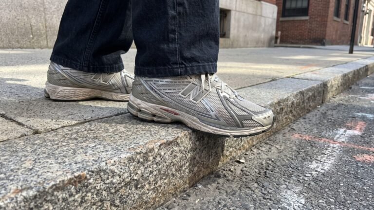 Worn silver New Balance 1906R sneakers on a granite city curb during an urban wear test