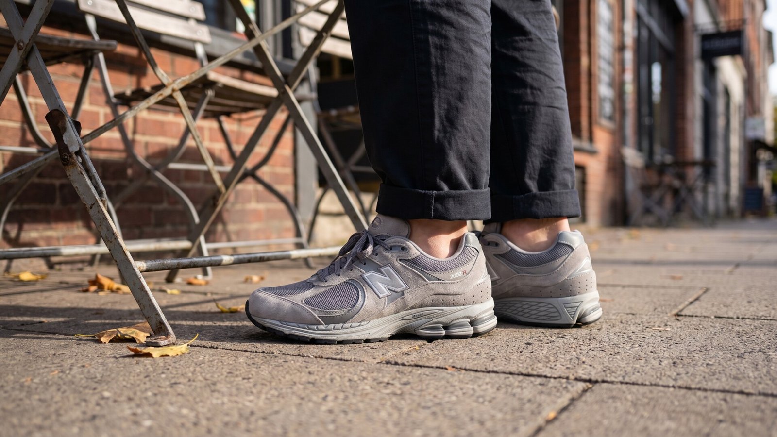Grey New Balance 2002R sneakers worn on foot with cuffed trousers on an urban sidewalk