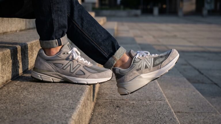 New Balance 990v4 and 990v6 grey sneakers worn on opposite feet while sitting on outdoor stone steps
