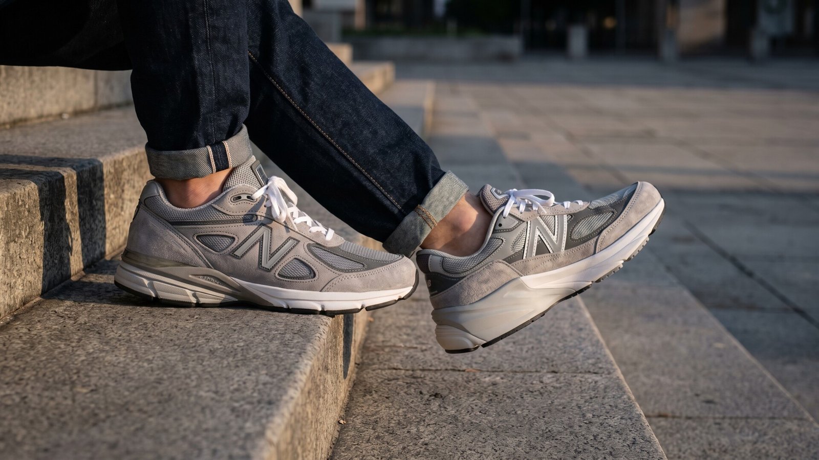 New Balance 990v4 and 990v6 grey sneakers worn on opposite feet while sitting on outdoor stone steps