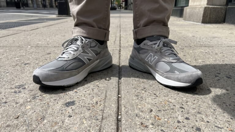 Side-by-side comparison of grey New Balance 990v6 and 993 sneakers worn on opposite feet on a city sidewalk