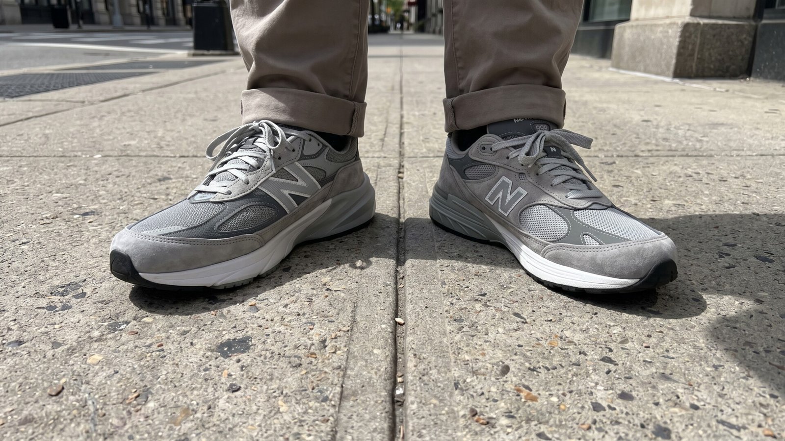 Side-by-side comparison of grey New Balance 990v6 and 993 sneakers worn on opposite feet on a city sidewalk