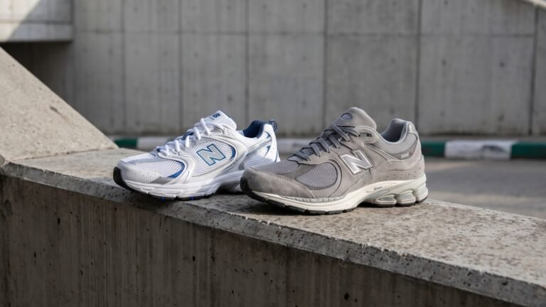 New Balance 530 in white and blue next to a grey New Balance 2002R sneaker on a concrete ledge