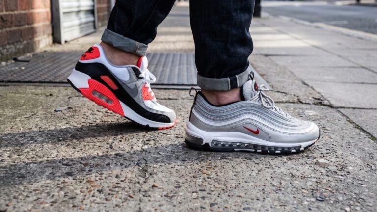 Nike Air Max 90 Infrared and Air Max 97 Silver Bullet worn on foot side by side on a sidewalk