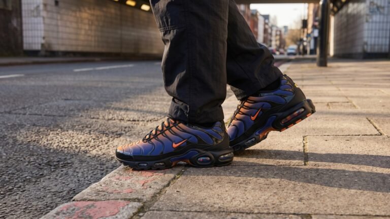 Nike Air Max Plus sneakers with blue and orange sunset gradient worn on an urban street curb