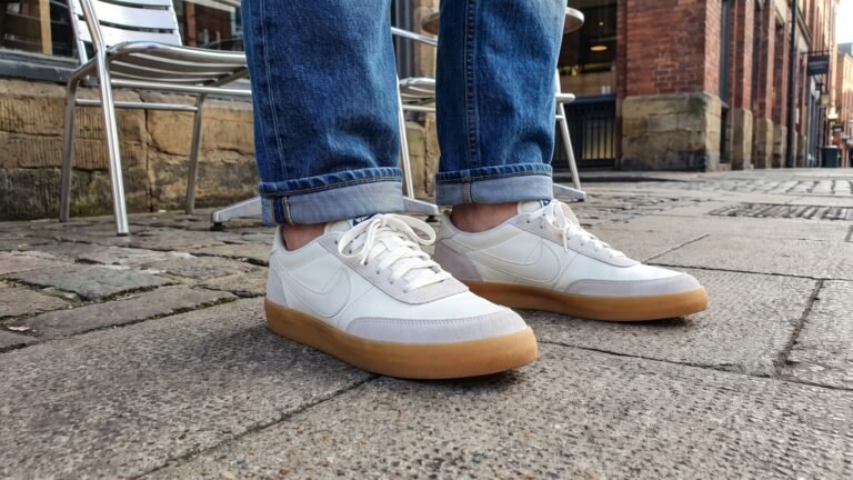 White Nike Killshot 2 sneakers with gum soles worn with cuffed blue jeans on an urban street