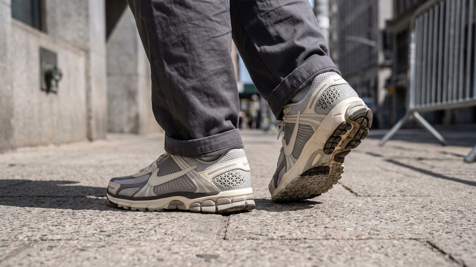 Low angle view of Nike Zoom Vomero 5 sneakers worn on foot while walking along a paved city sidewalk