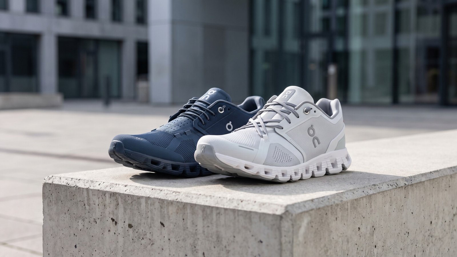 Navy and light grey On Cloud running shoes side by side on an outdoor concrete ledge