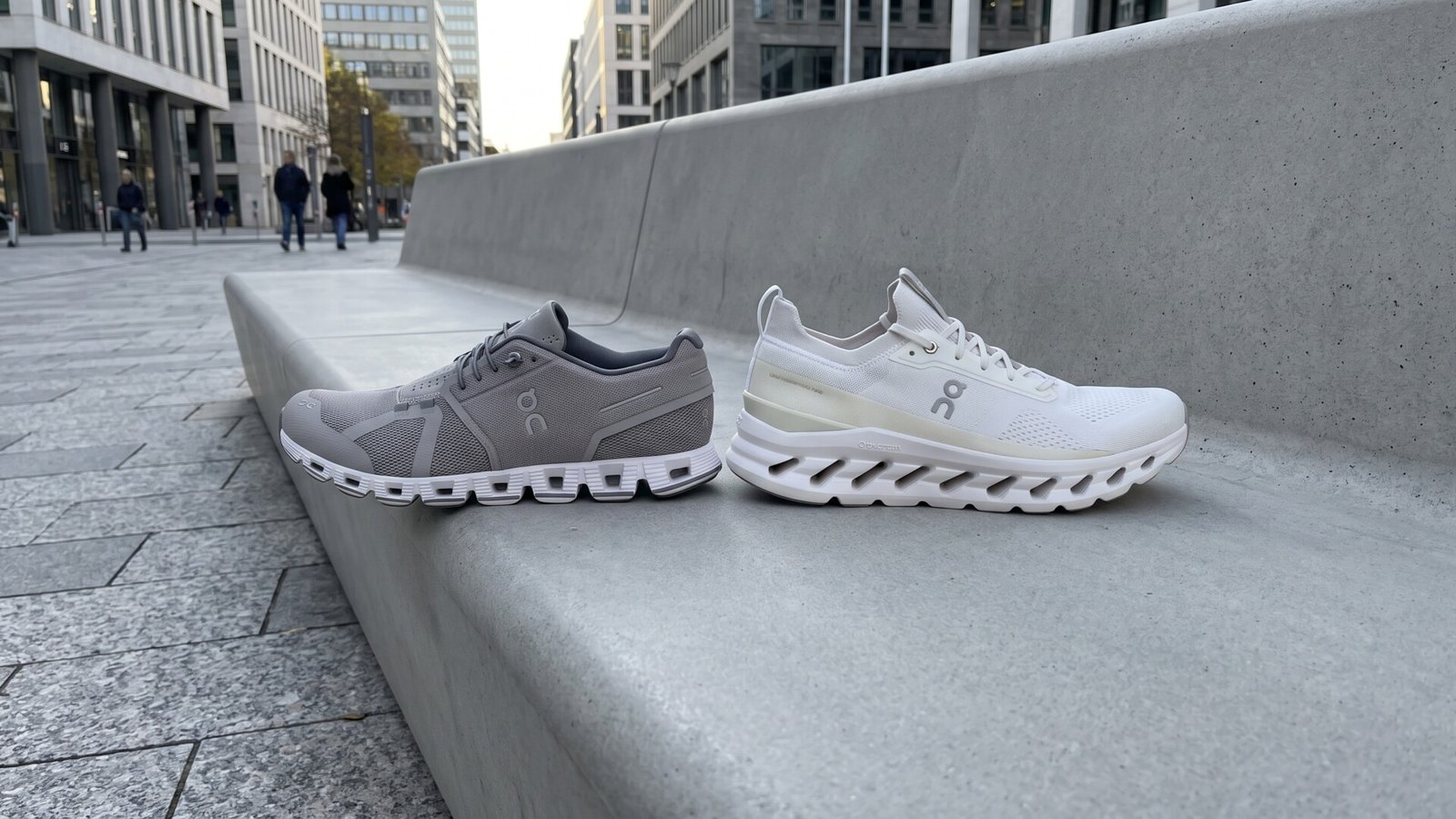 Side profile of a grey On Cloud 5 next to a white On Cloudtilt sneaker on an outdoor concrete bench
