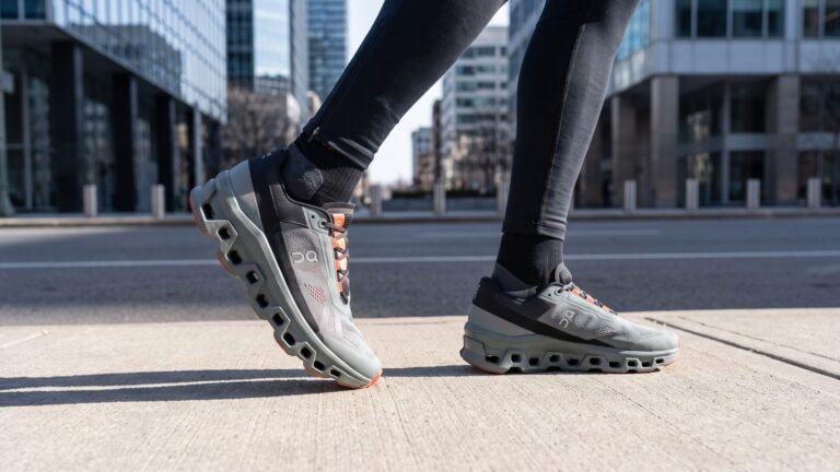 Runner wearing grey and orange On Cloudmonster shoes mid-stride on a city sidewalk