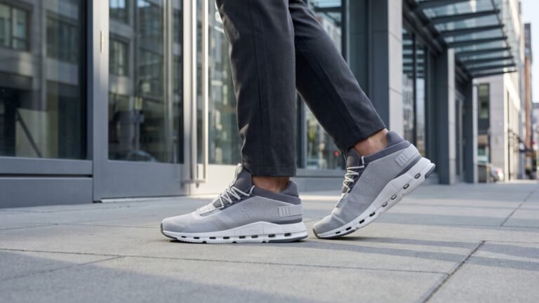 Side view of grey On Cloudnova sneakers worn with trousers while walking down a paved city street