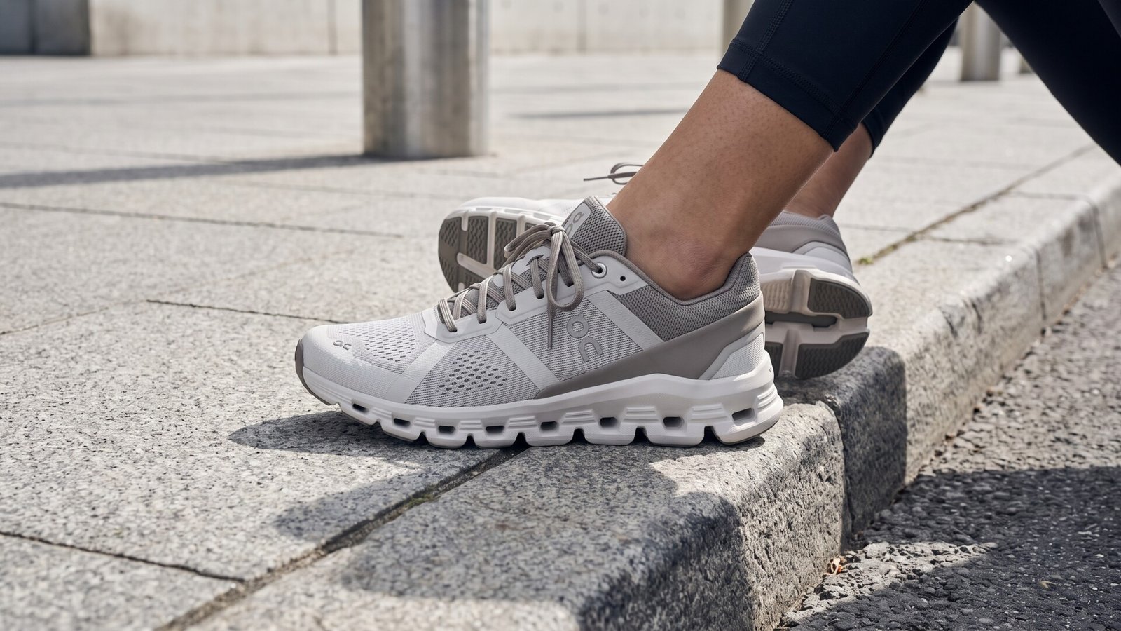 Close-up of grey and white On Cloudrunner running shoes resting on a concrete city curb