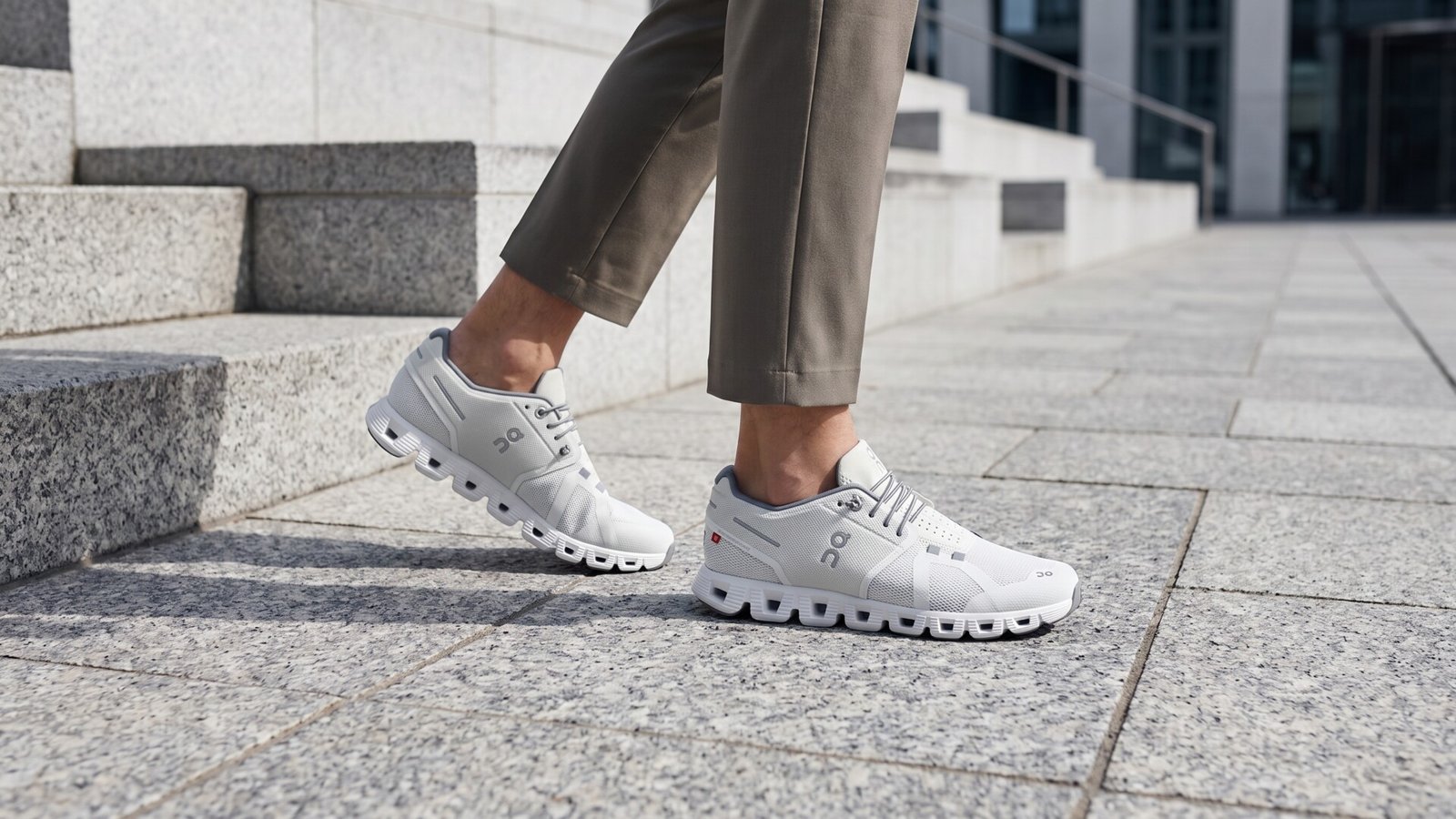 Person wearing white On running sneakers and cropped trousers walking across a light stone plaza
