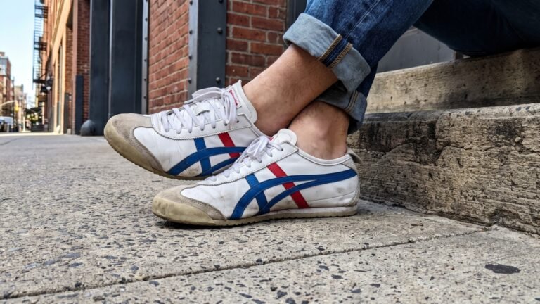 Broken-in white Onitsuka Tiger Mexico 66 sneakers with blue and red stripes worn with cuffed jeans on a sidewalk