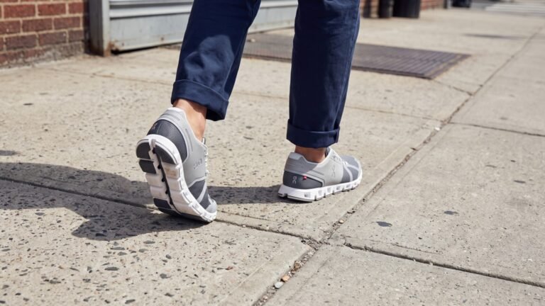Close-up of a person walking on a sidewalk wearing grey On Cloud sneakers with cushioned soles